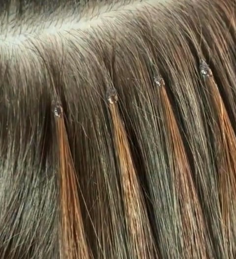 Back view of a woman with long wavy platinum-blonde hair with a black bow, demonstrating the length and movement achievable with keratin bond extensions in London.